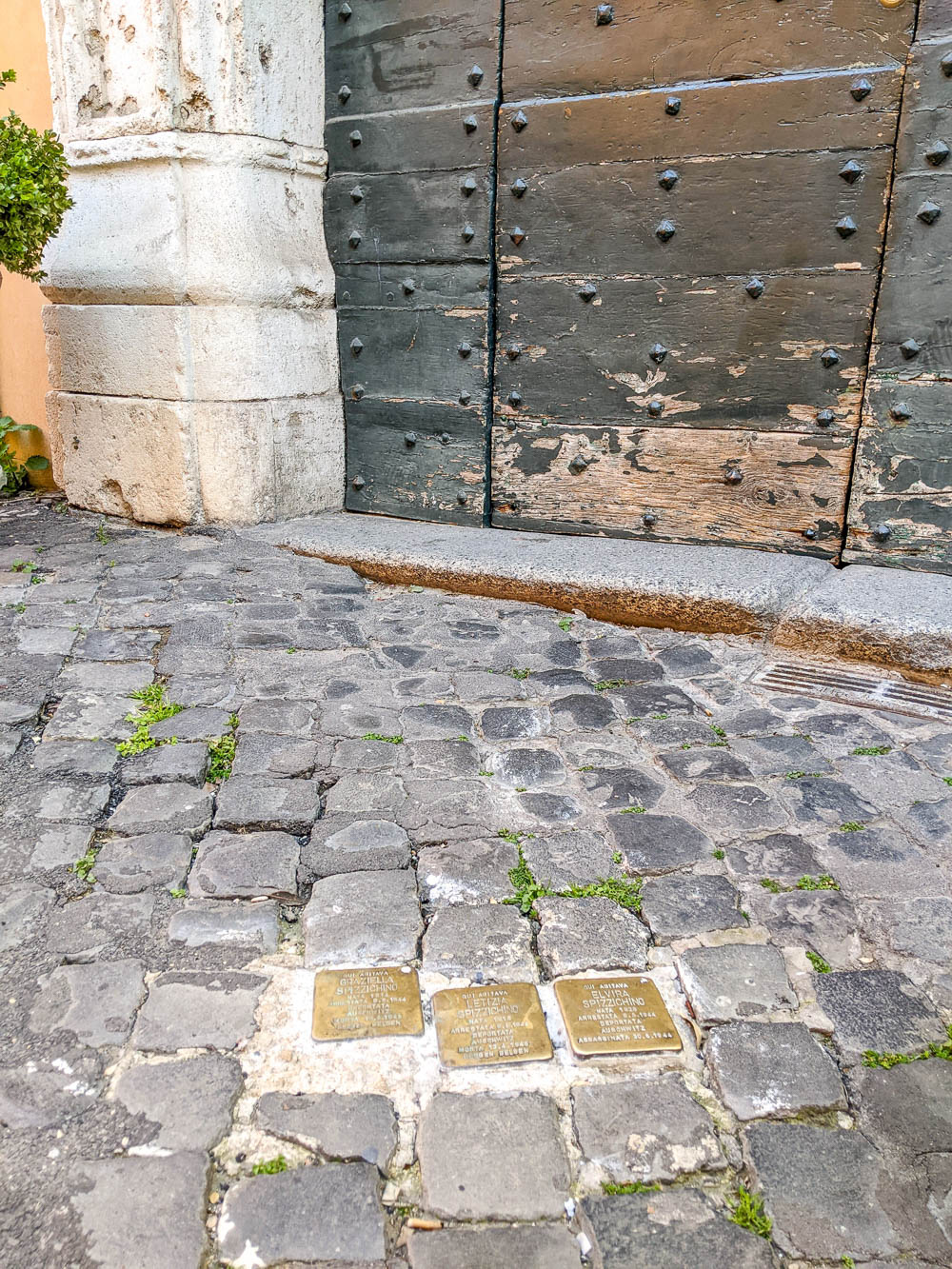 three brass cobblestones inlaid into the street with names and information on them in front of a door