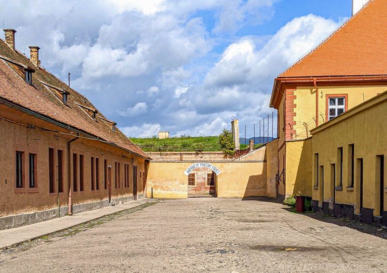 old brick buildings painted yellow with orange roof and Arbeit Macht Frei sign in the middle