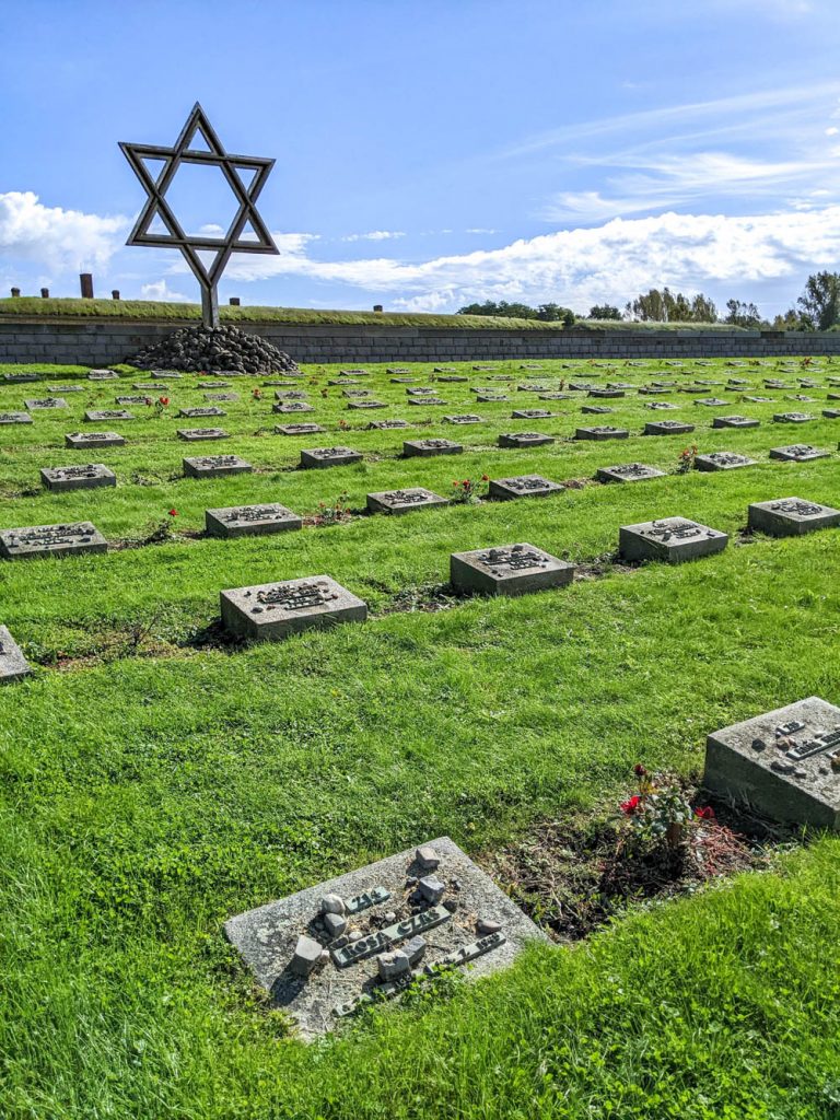 large cemetery with lots of rows of gravestones on green grass in front of a giant star of david