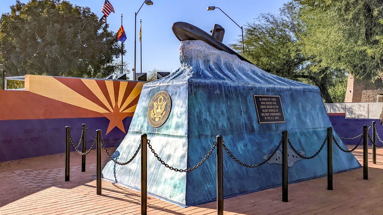 blue monument that looks like an ocean wave with a submarine on top in front of wall painted like arizona flag