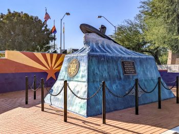 blue monument that looks like an ocean wave with a submarine on top in front of wall painted like arizona flag
