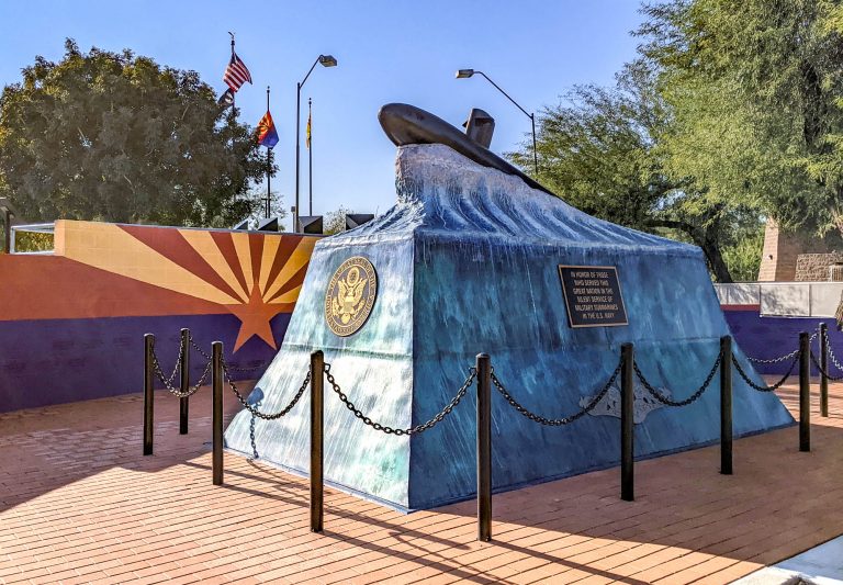 blue monument that looks like an ocean wave with a submarine on top in front of wall painted like arizona flag