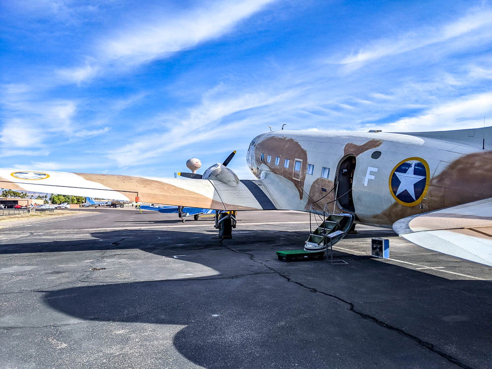 exterior of C-47 airplane painted brown camouflage under a blue sky