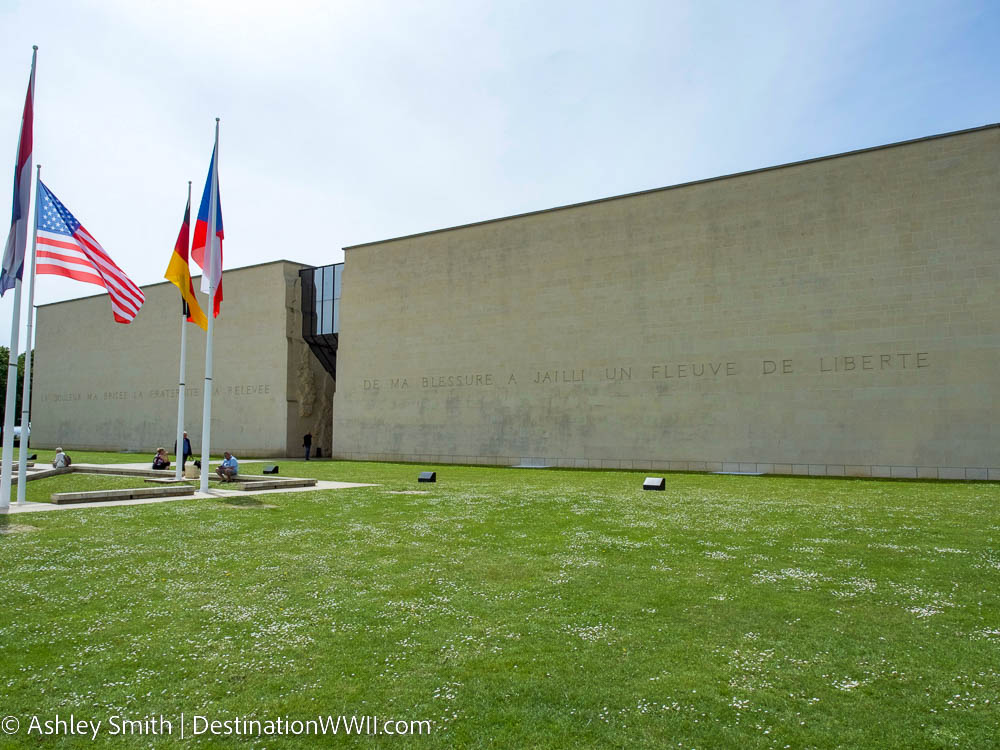 exterior of caen museum - large concrete wall with flags in front