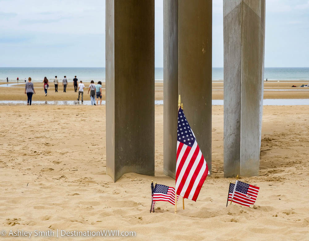 small american flags in front of a steel memorial on a beach