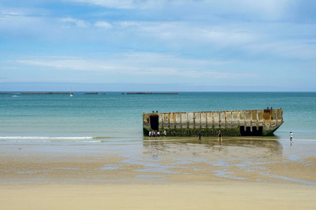 artifical harbor of arromanches sitting in a teal ocean