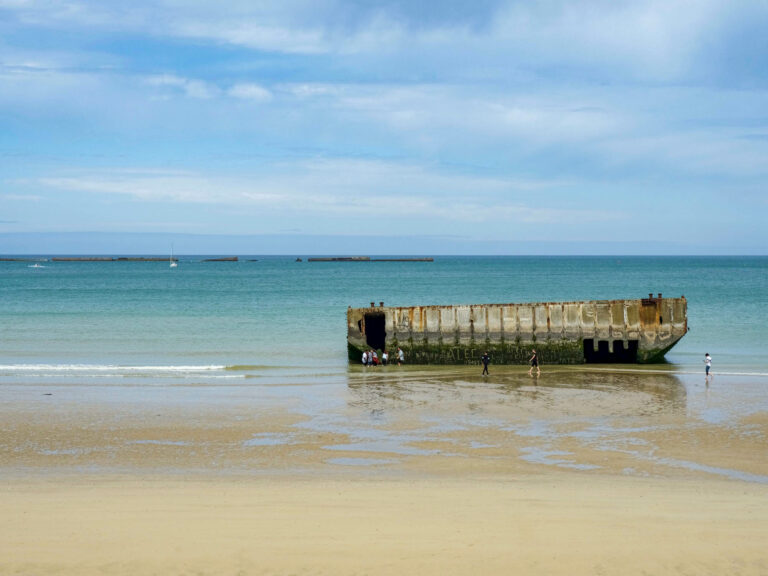 artifical harbor of arromanches sitting in a teal ocean