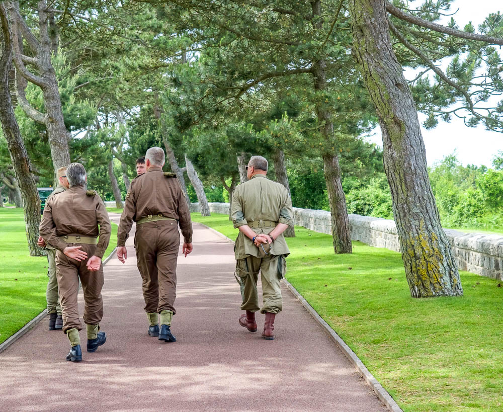 three men in wwii uniforms walking through a cemetery