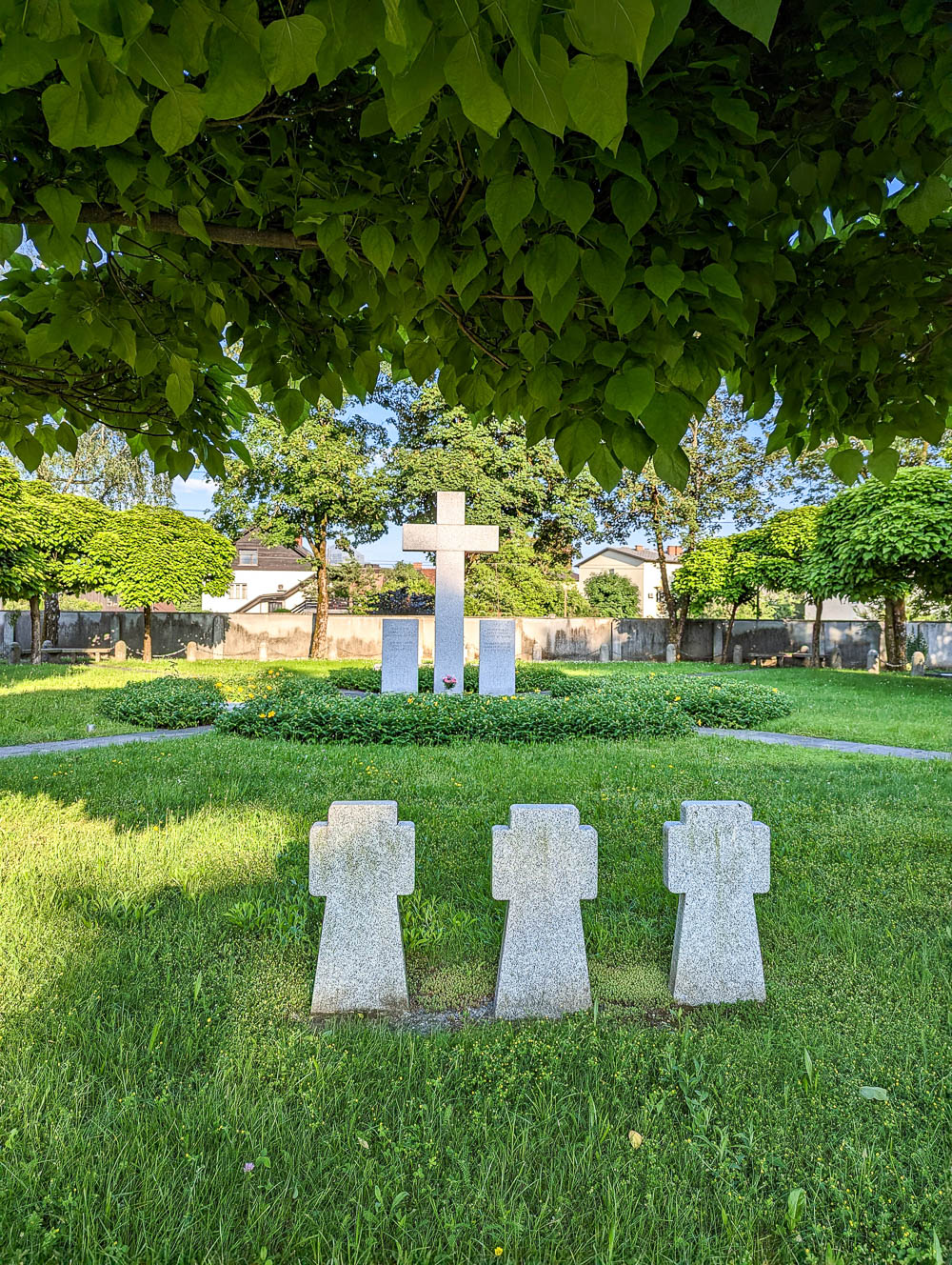 large cross memorial and small cross grave markers under a tree