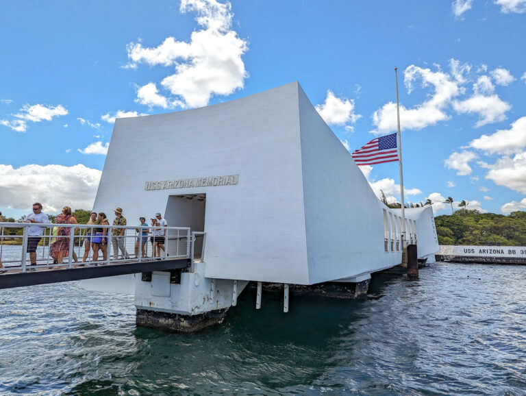 people walking out of a white memorial over the ocean