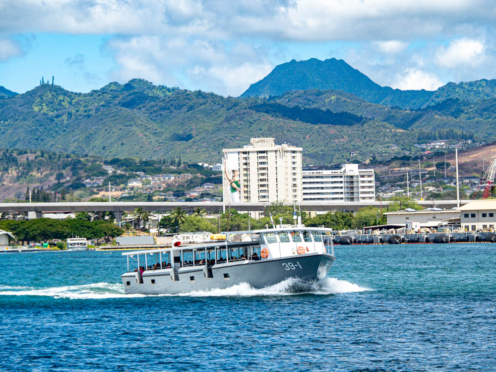 fast moving shuttle boat in the ocean in front of a shore with mountains and buildings