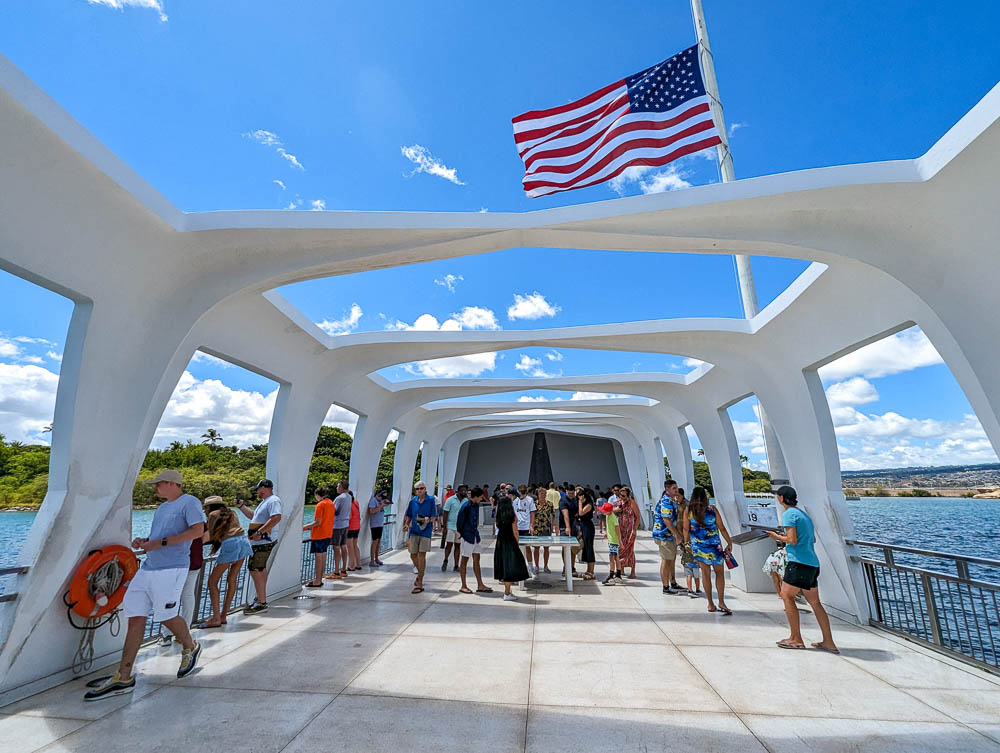 people standing in a white memorial building over the ocean under an american flag