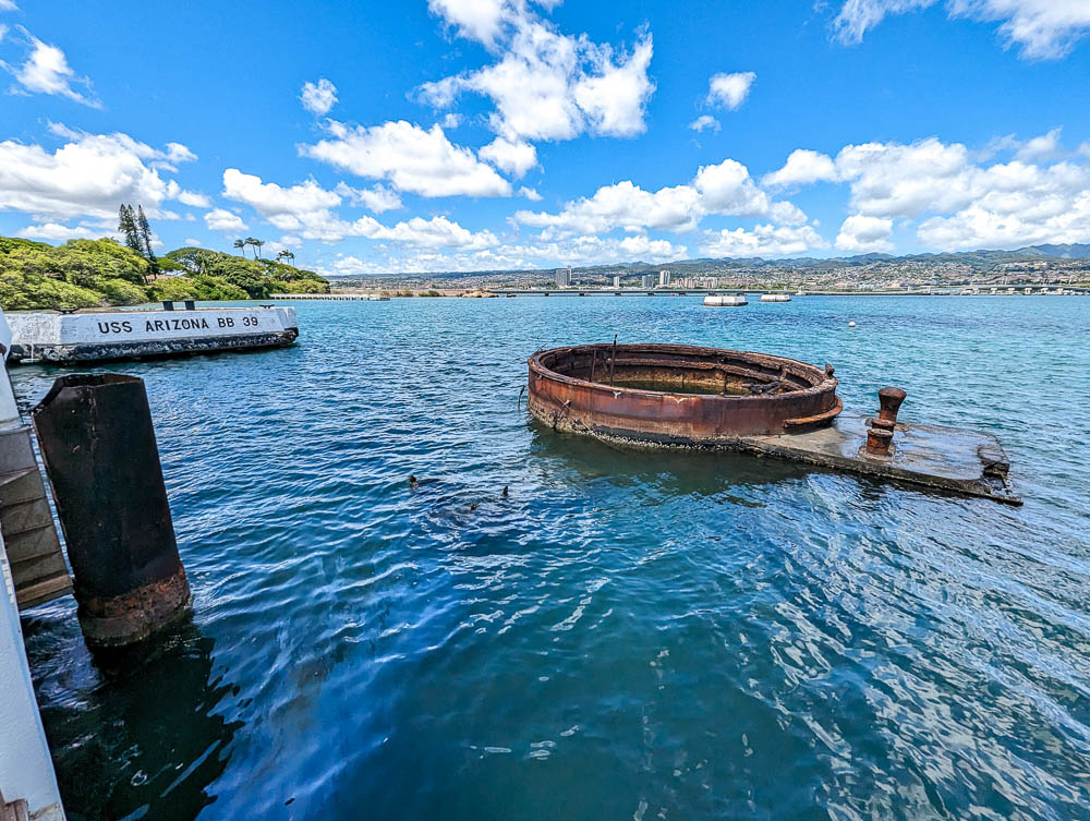 rusted part of a ship sticking out of the water surrounded by oil and water