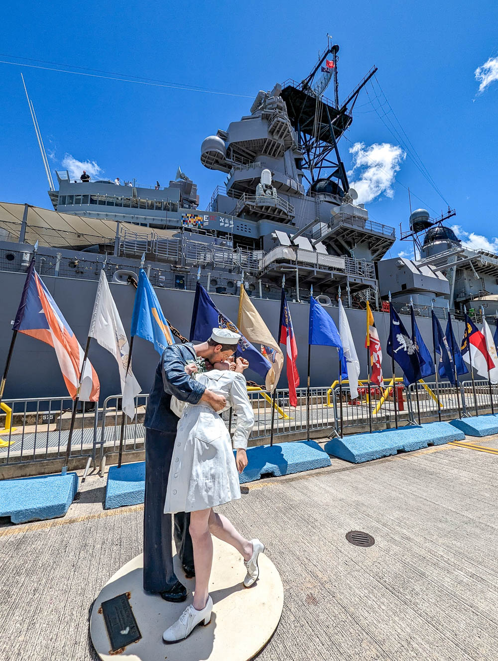 statue of a man kissing a women in front of a battleship and lots of country flags