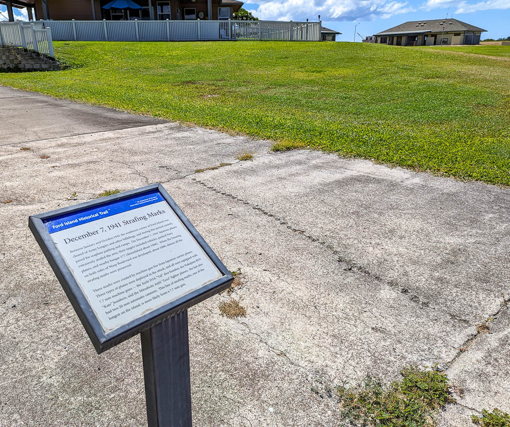 informational sign about pearl harbor strafing marks next to a sidewalk with holes in it