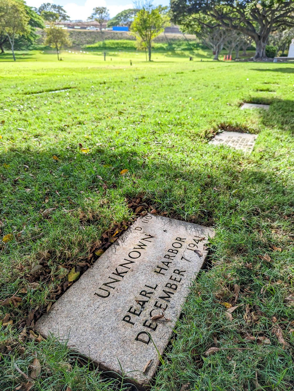 grave marker of pearl harbor victim that says unknown and is surrounded by green grass
