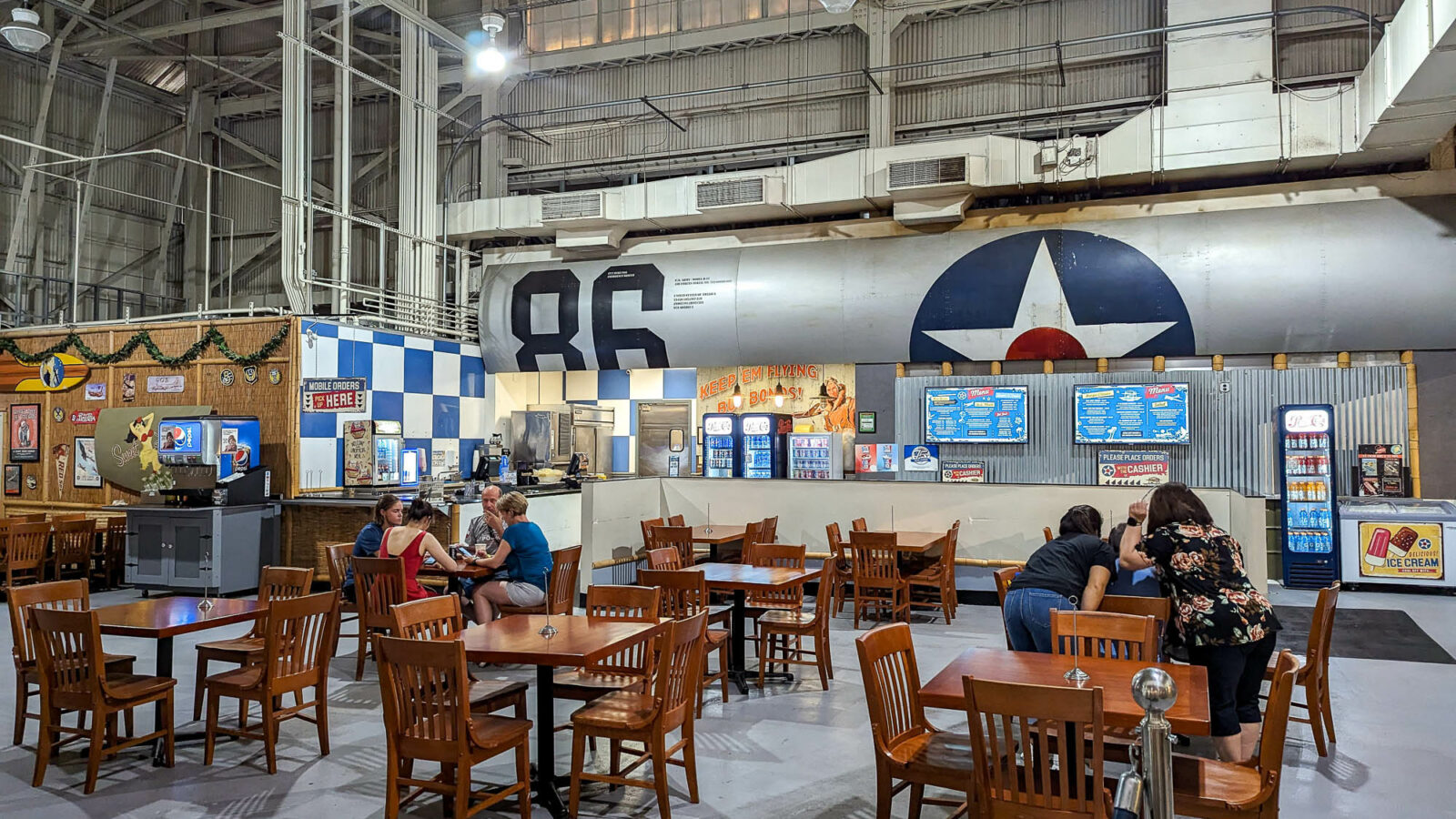 people sitting at brown tables inside an airplane hangar