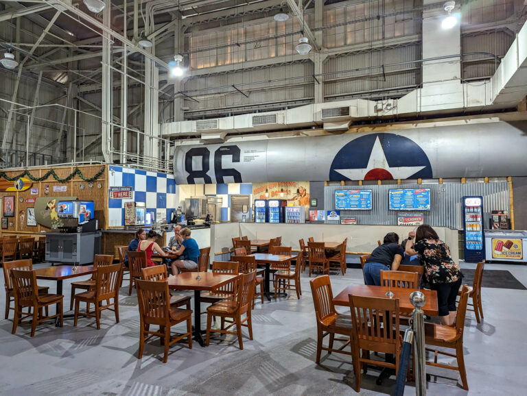 people sitting at brown tables inside an airplane hangar