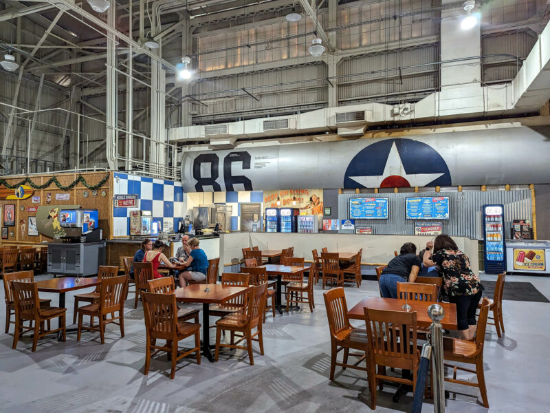 people sitting at brown tables inside an airplane hangar