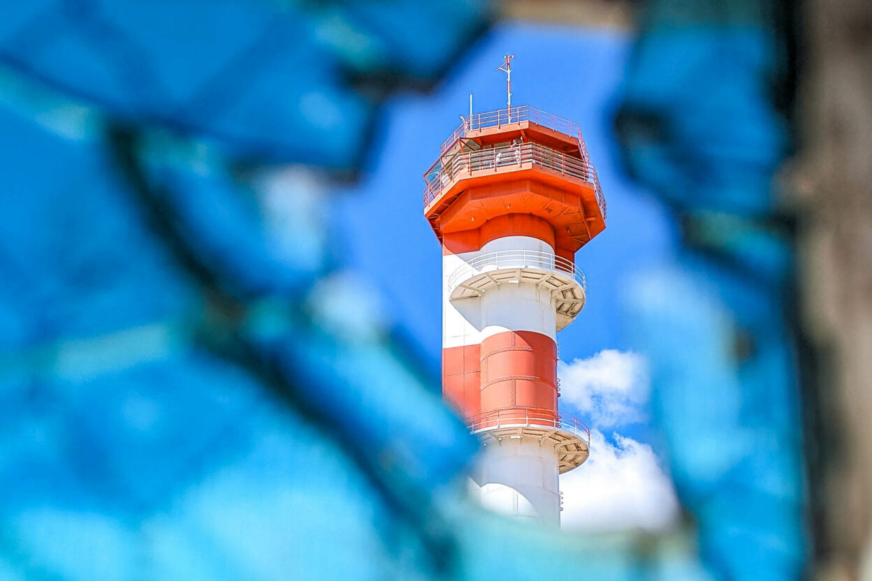 View of red and white striped control tower through broken blue glass