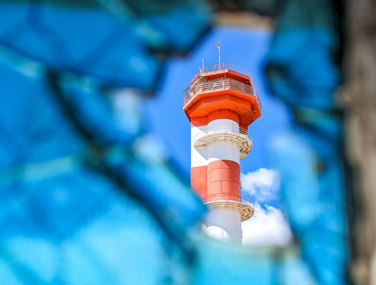 View of red and white striped control tower through broken blue glass