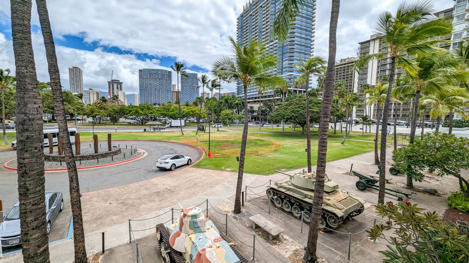 camouflage wwii tanks sitting under palm trees outside a museum